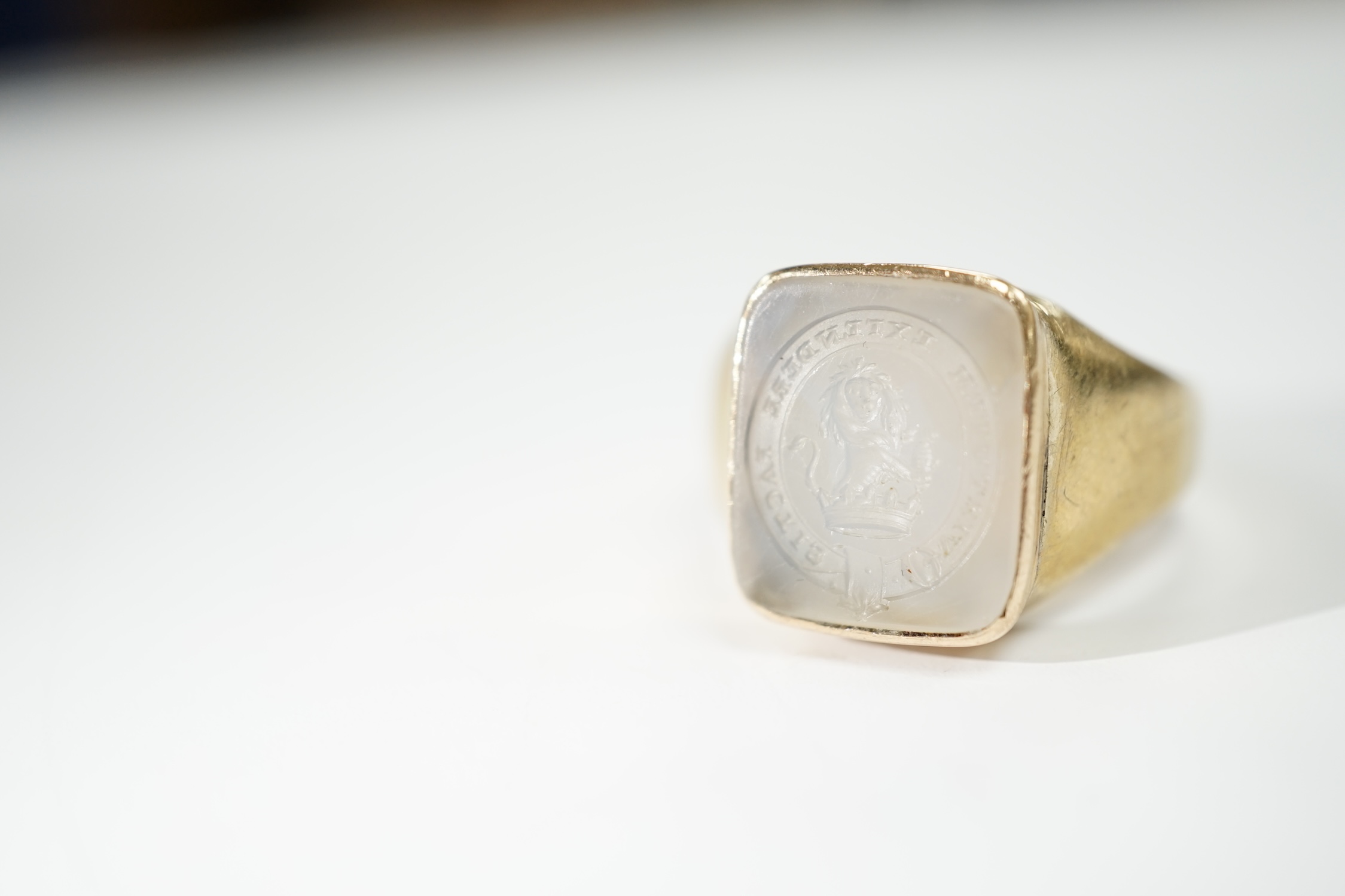 An early 20th century yellow metal and white chalcedony intaglio ring, the matrix carved with the motto 'Virtutum Extendere Factis' with crest, size W, gross weight 9.4 grams.